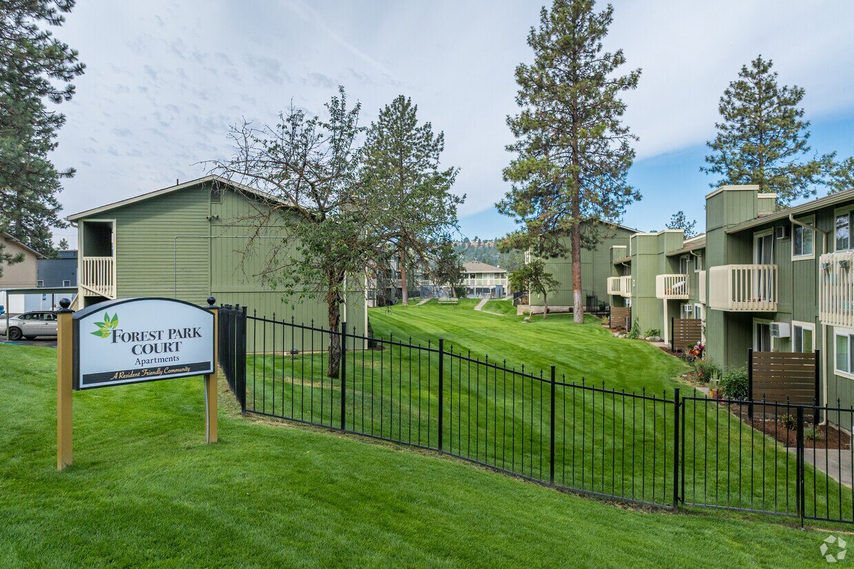 A sign for Forest Park Courtyard Apartments is in front of a black fence.
